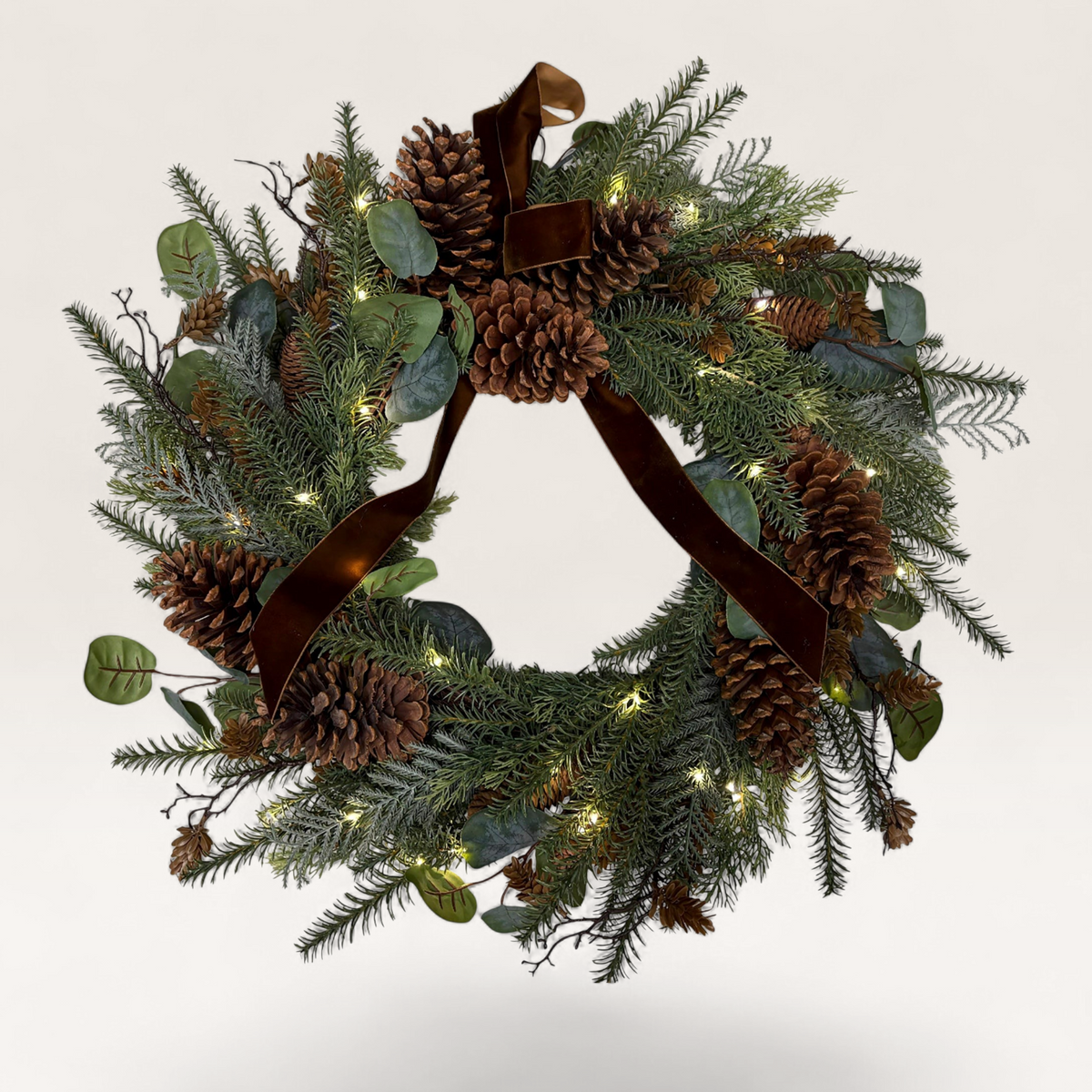 Vintage Industrial Kuta Christmas wreath with green PVC foliage, pinecones, warm LED lights, and a brown velvet ribbon.