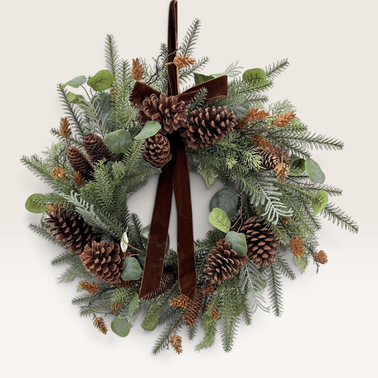 Vintage Industrial Corona Kuta green PVC Christmas wreath with pinecones and a brown velvet ribbon on a light wall